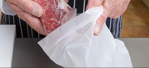 Butcher putting meat into white counter bag.