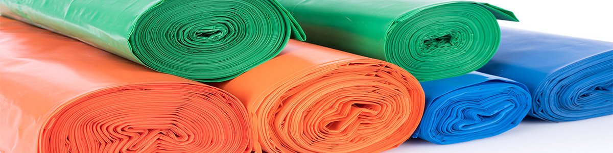 Multicoloured green, red, orange and blue refuse sack rolls stacked on top of each other.