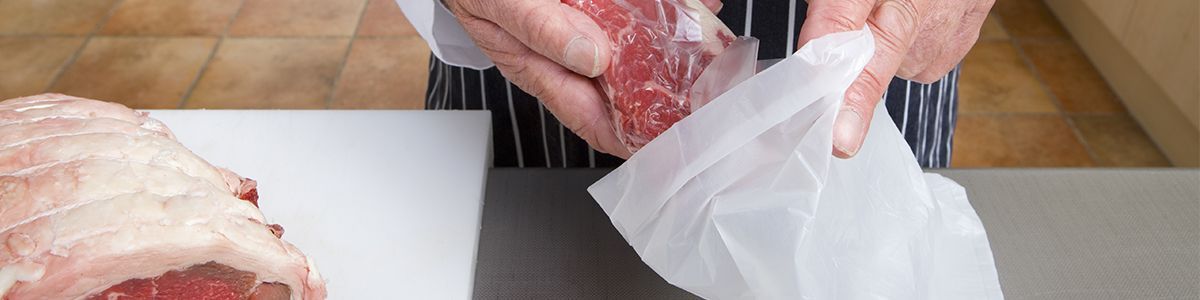 Butcher packaging meat into a white counter bag.