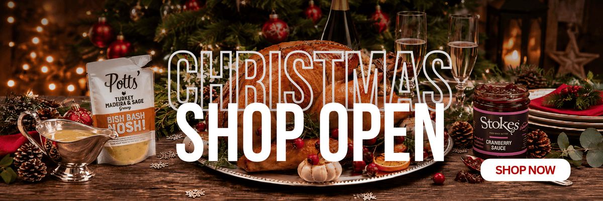 A festive Christmas-themed promotional banner with large text reading 'CHRISTMAS SHOP OPEN' over a decorated table scene. Visible products include a bag of Pots' Christmas Punch and a jar of Stokes Christmas Punch on a wooden table with candles, glasses, pinecones, and holiday decor in the background.