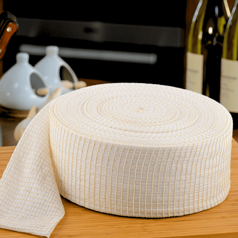 A roll of textured white kitchen meat netting with a grid pattern, partially unrolled on a wooden surface with kitchen items blurred in the background.