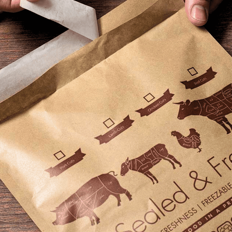 A close-up of a kraft paper food storage bag being opened by hands, with printed butcher-style animal illustrations and labels on the front.